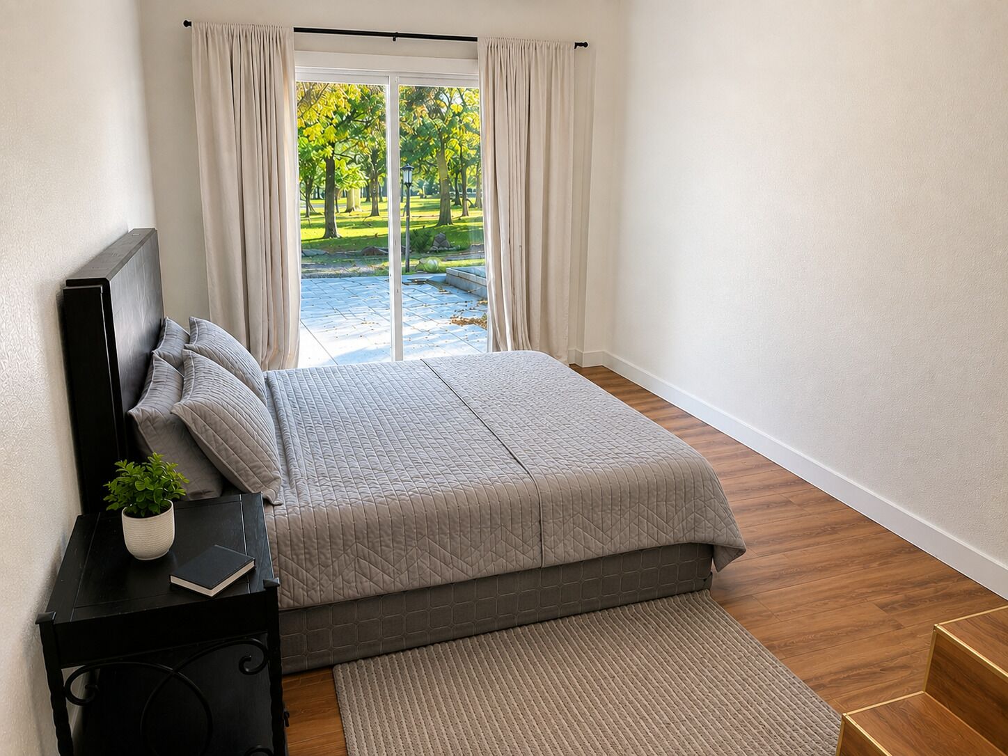Une chambre à coucher avec un lit, une table de chevet ornée d’une plante, une fenêtre avec des rideaux et une vue sur un jardin.