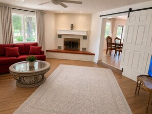 A living room with a red sofa, a glass coffee table, a fireplace, and a dining area with wooden furniture.