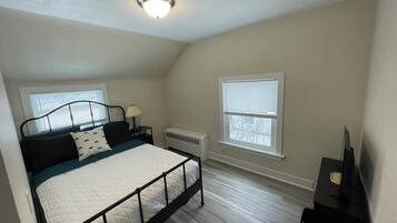 Une chambre à coucher avec un lit, une table de chevet, une lampe, un radiateur et une fenêtre.