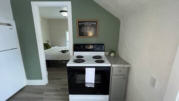 Une cuisine compacte avec un poêle blanc, un petit plan de travail et une porte donnant sur une chambre.