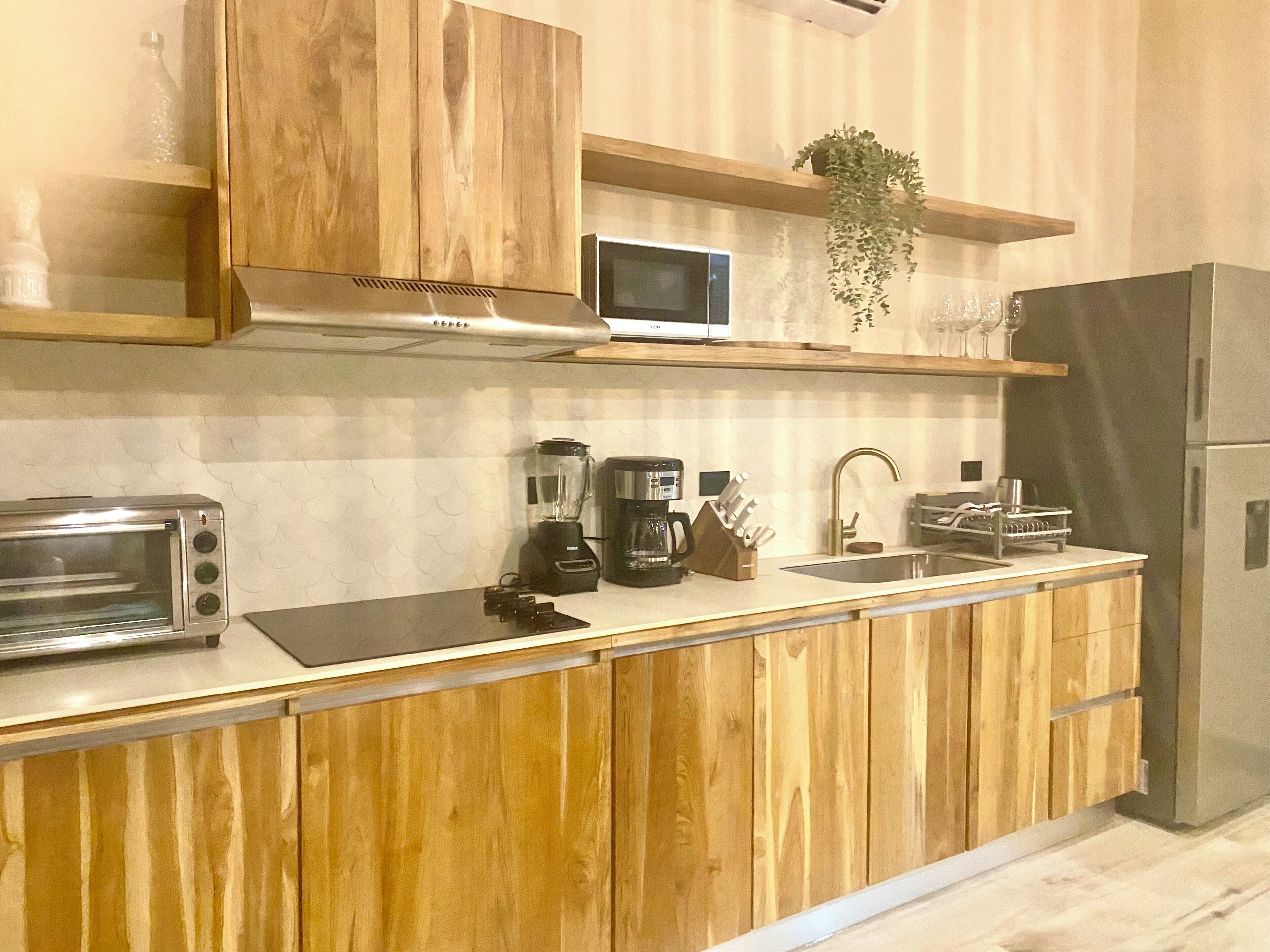 Een moderne keuken met houten kastjes, een ingebouwde magnetron, een koffiezetapparaat en een koelkast.