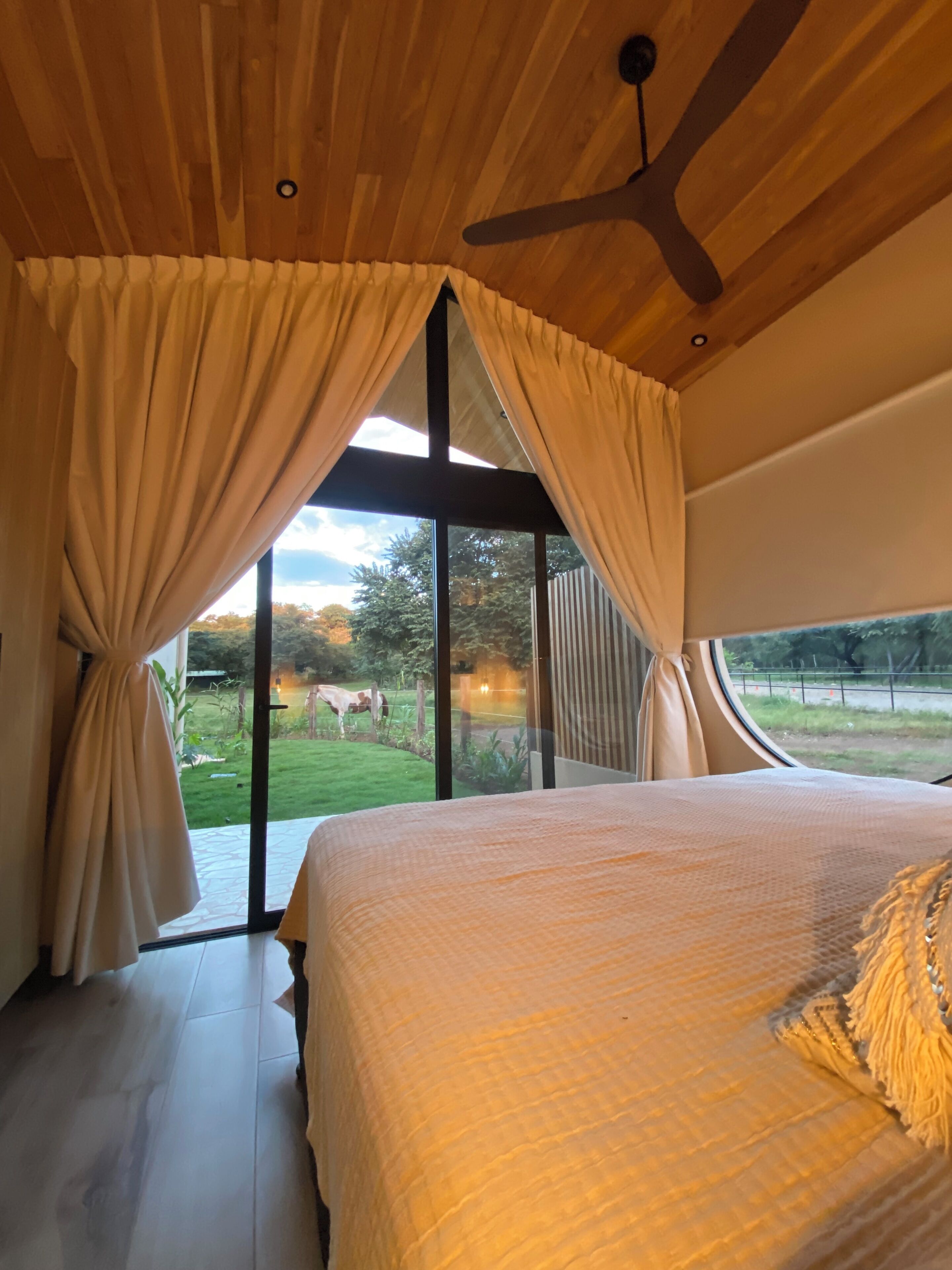 A bedroom with a large bed, curtains, and a view of a green landscape.