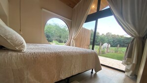 Ein Schlafzimmer mit einem großen Bett, einem Rundfenster und Blick ins Freie.