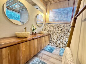 A bathroom with a wooden vanity, two round mirrors, a stone wall, and a window with blinds. - Villa Paraíso Jacques - Private Pool, Horses and beach (Provincia de Guanacaste)