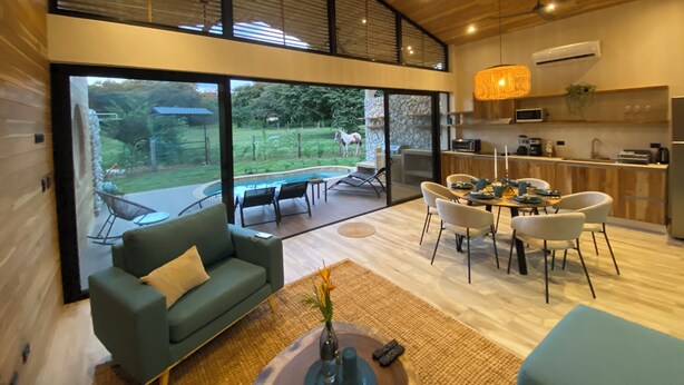 Ein modernes Interieur mit Essbereich, einer Couch, einer Küche und Blick ins Freie.