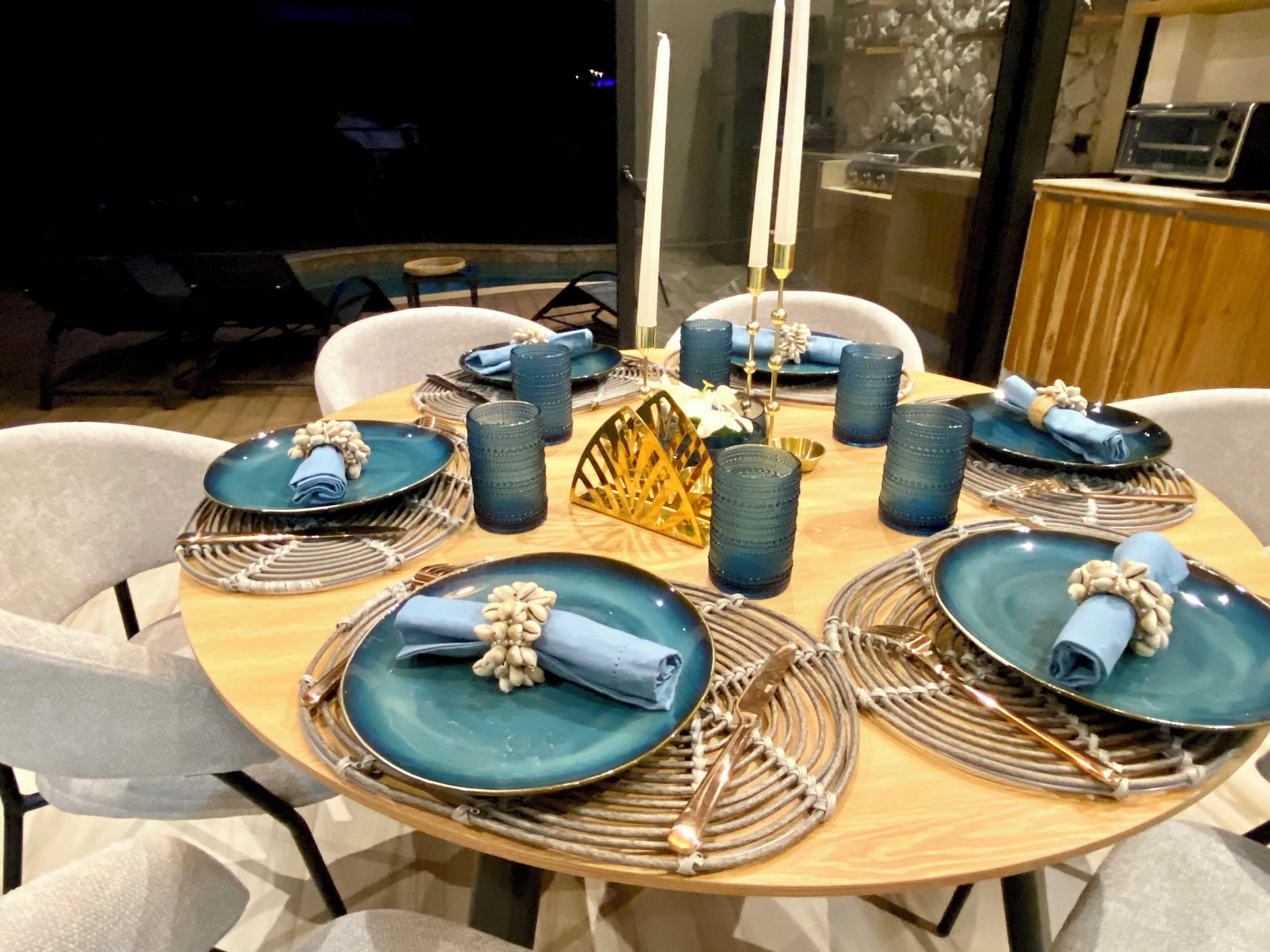 Een ronde eettafel met blauwe borden, servetten en decoratieve objecten.