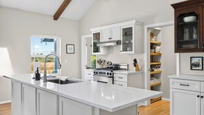 A kitchen with white cabinetry, a large island, stainless steel appliances, and a view of a field through a window. - Edgefield Farmhouse by Avantstay Hot Tub + Firepit + 5 Private Acres Trailhead + Forts Nearby (Coupeville)