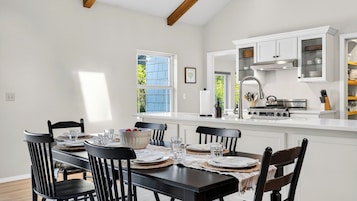Un coin repas avec une table dressée pour quatre personnes, une cuisine avec des meubles blancs et une fenêtre donnant sur un paysage verdoyant.