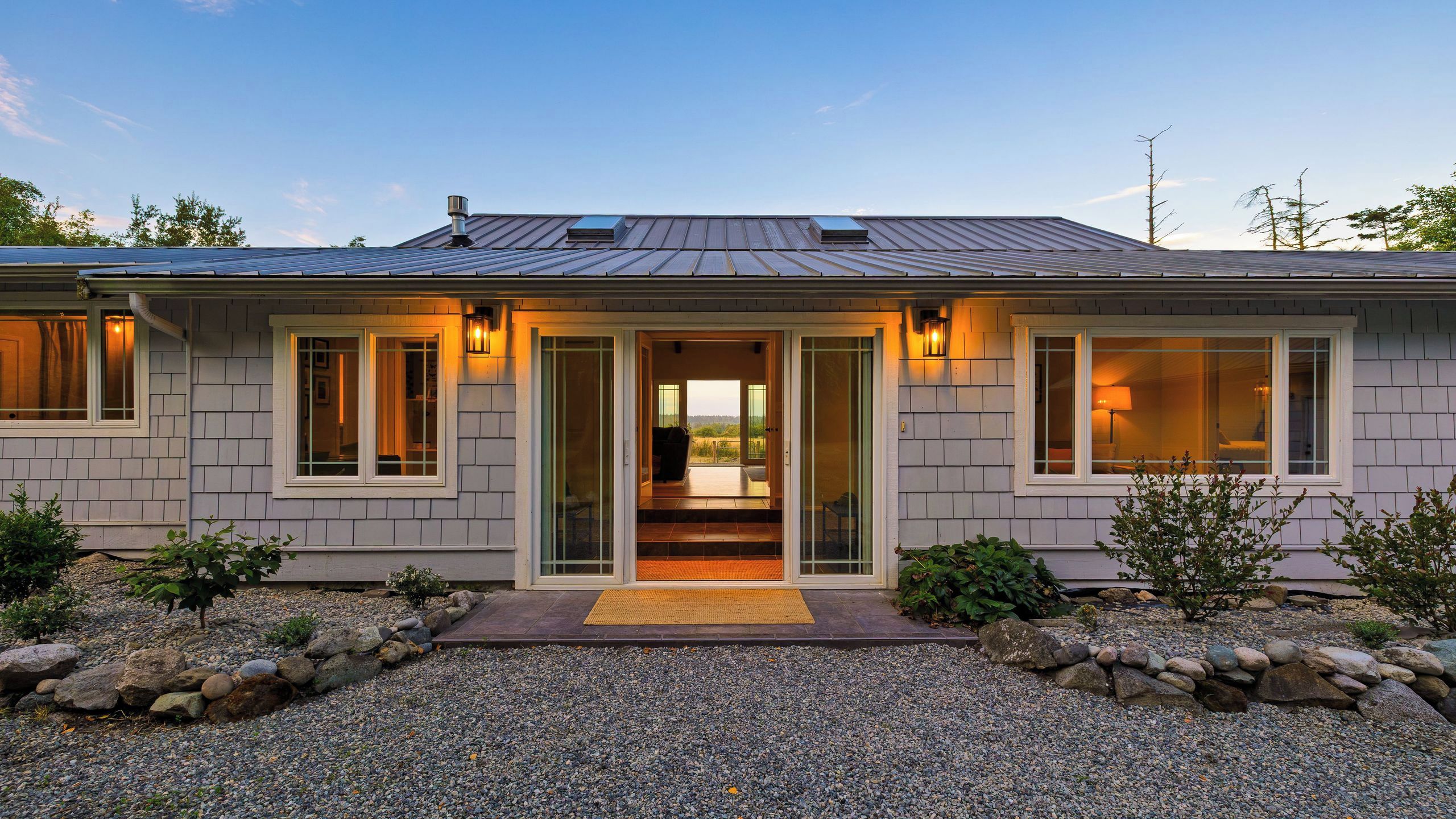A modern house with a covered entryway, large windows, and a gravel driveway.