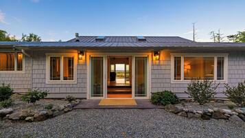 A modern house with a covered entryway, large windows, and a gravel driveway.