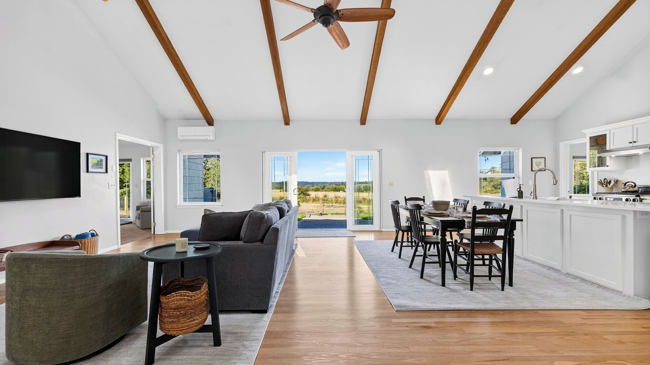 A spacious living area with a sofa, dining table, and chairs, a television, and a ceiling fan.
