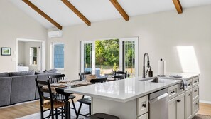A modern kitchen with a large island, a dining area with chairs, a sofa, and a view of the outdoors. - Edgefield Farmhouse by Avantstay Hot Tub + Firepit + 5 Private Acres Trailhead + Forts Nearby (Coupeville)