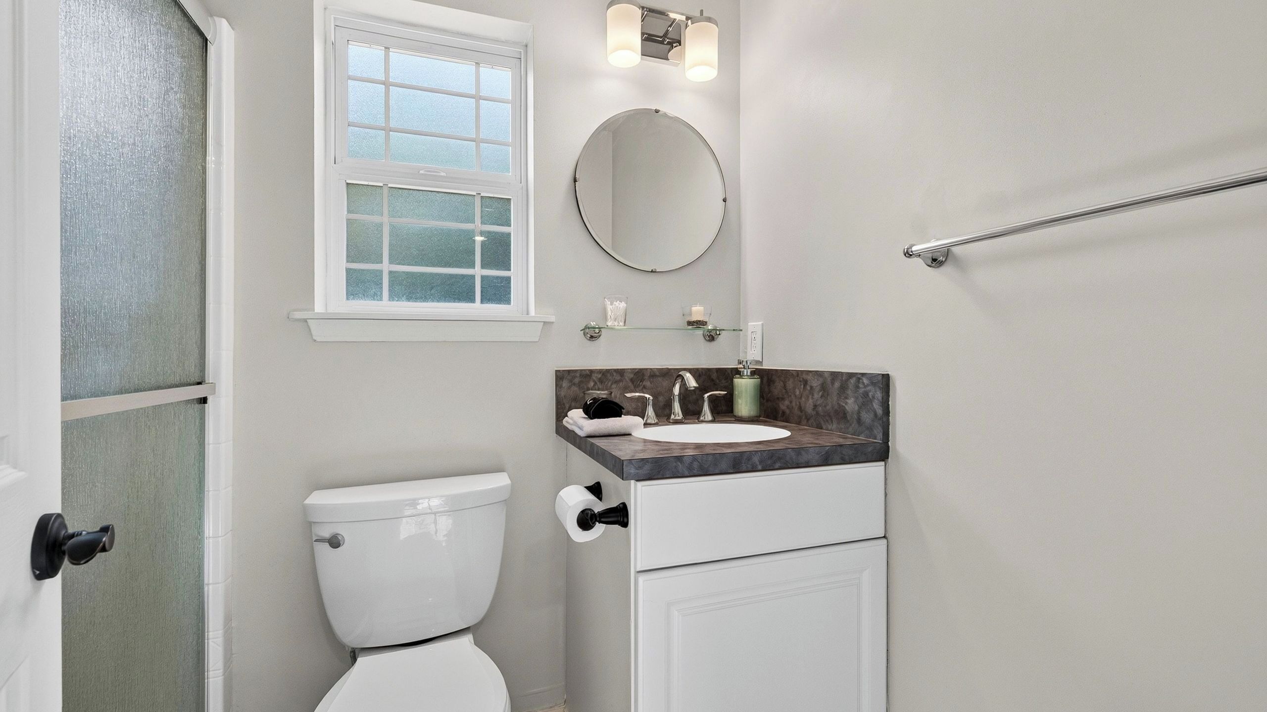 A bathroom with a toilet, sink, mirror, and window.