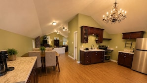 A spacious kitchen with wooden cabinets, a stainless steel refrigerator, and a dining area with a table and chairs. - The Good Neighbor’s Loft (Orrstown)