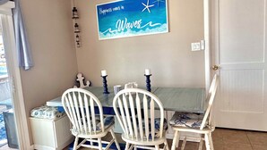 A dining area with a table and four chairs, a wall-mounted sign, and a door. - Mystic Island Lagoon Front Escape with Private Dock and Hot Tub ⚓️☀️ (Little Egg Harbor Township)
