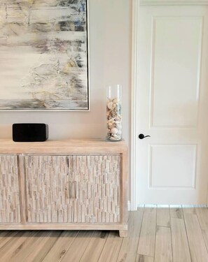 A wooden console with a black object on top, a glass vase with stones, and a painting on the wall. - Luxury Coastal Retreat - Beach & Lagoon (Carlsbad)