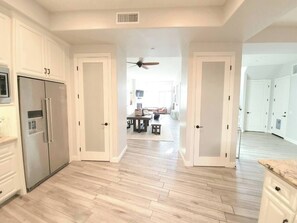 A spacious kitchen with white cabinetry, a stainless steel refrigerator, and a wooden floor. - Luxury Coastal Retreat - Beach & Lagoon (Carlsbad)