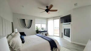 Ein Schlafzimmer mit Bett, Nachttisch, Lampe, Deckenventilator und Kamin.