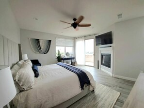 A bedroom with a bed, bedside table, lamp, ceiling fan, and a fireplace. - Luxury Coastal Retreat - Beach & Lagoon (Carlsbad)