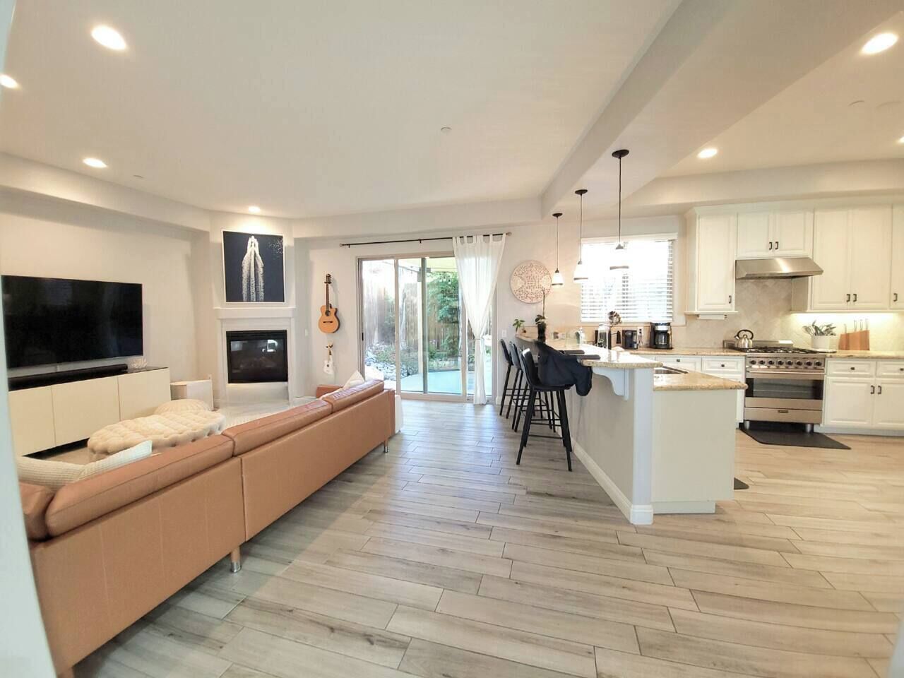 Una cocina moderna con una isla central, un comedor con taburetes de bar y una sala de estar con un televisor grande y un sofá.