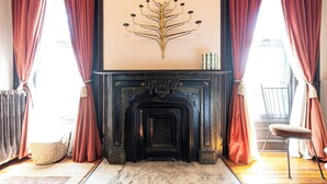 Um quarto com lareira, cortinas, um cesto de palha e uma cadeira.
