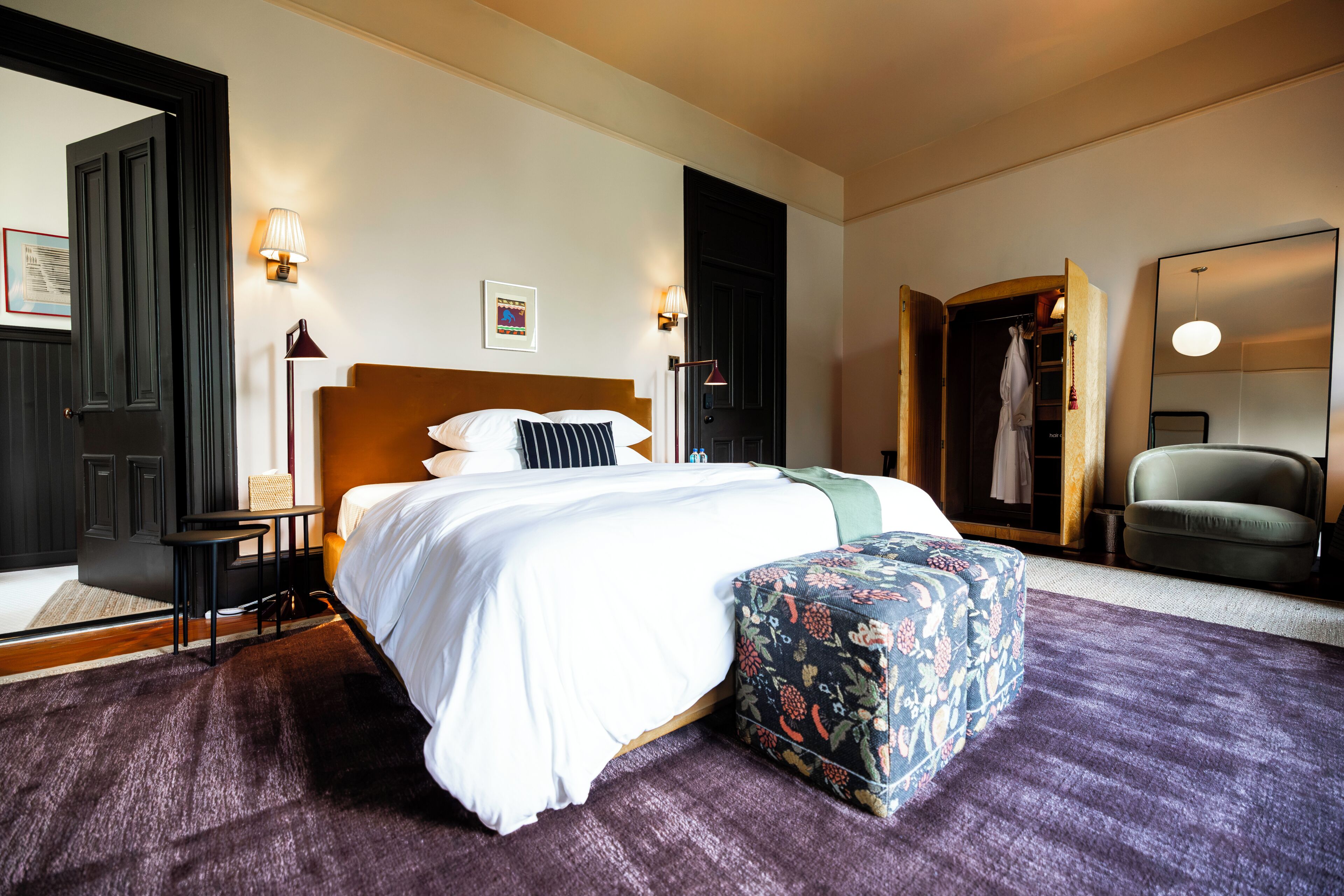 A hotel room with a large bed, bedside tables, a chair, a mirror, and a door.