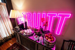 Una zona de bar con un letrero de neón, una lámpara y diferentes alimentos y bebidas.