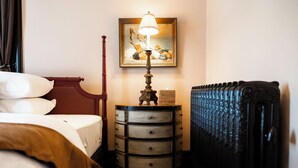A room with a bed, a nightstand with a lamp, a painting on the wall, and a radiator. - Truitt Hotel (St. Louis)