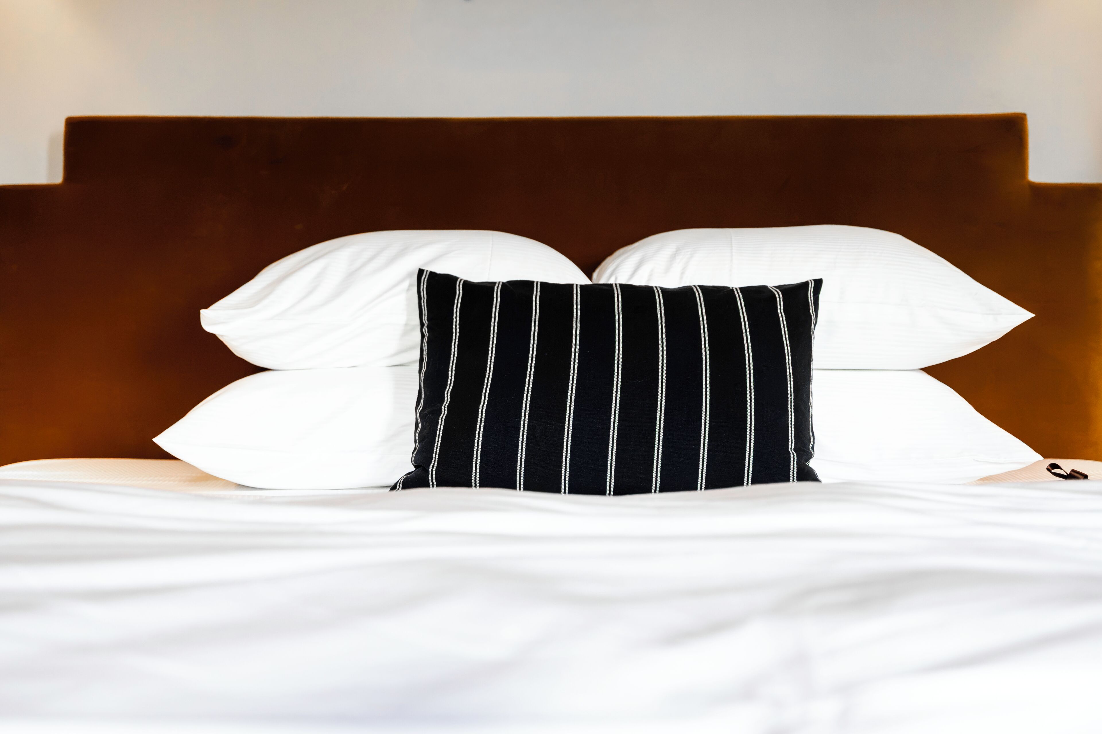 Een bed met wit beddengoed en een zwart-wit gestreept kussen.