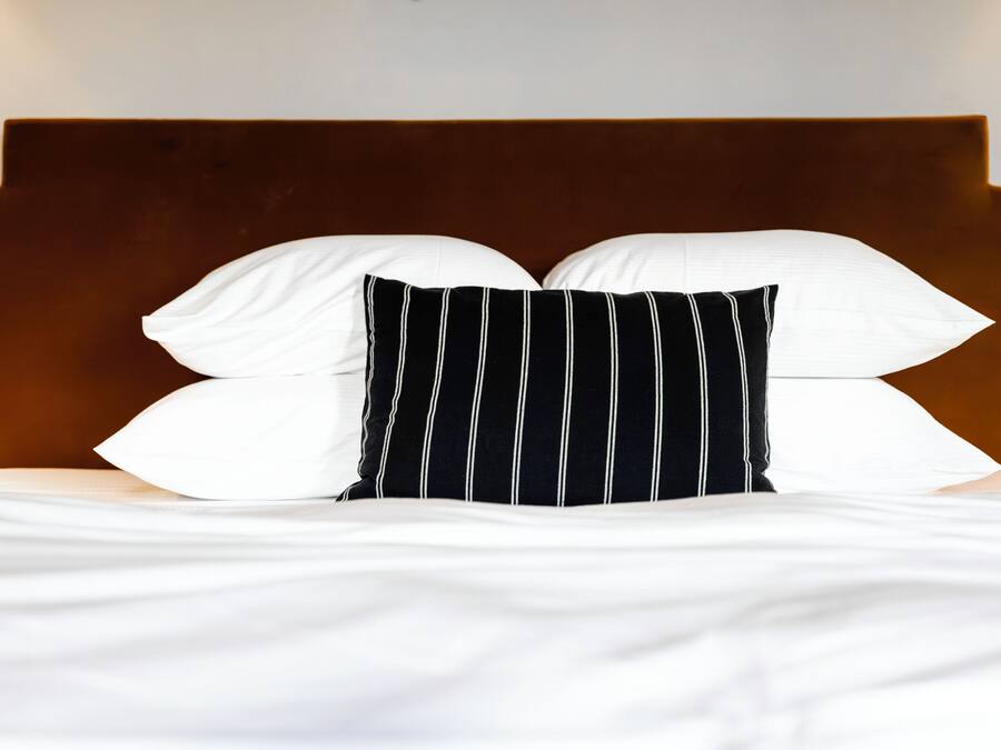 Een bed met wit beddengoed en een zwart-wit gestreept kussen.