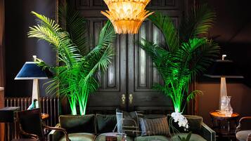 A room with a dark wooden door, a chandelier, green plants, and a seating area with a sofa and chairs.