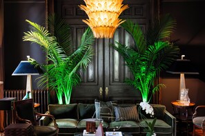 A room with a dark wooden door, a chandelier, green plants, and a seating area with a sofa and chairs. - Truitt Hotel (St. Louis)