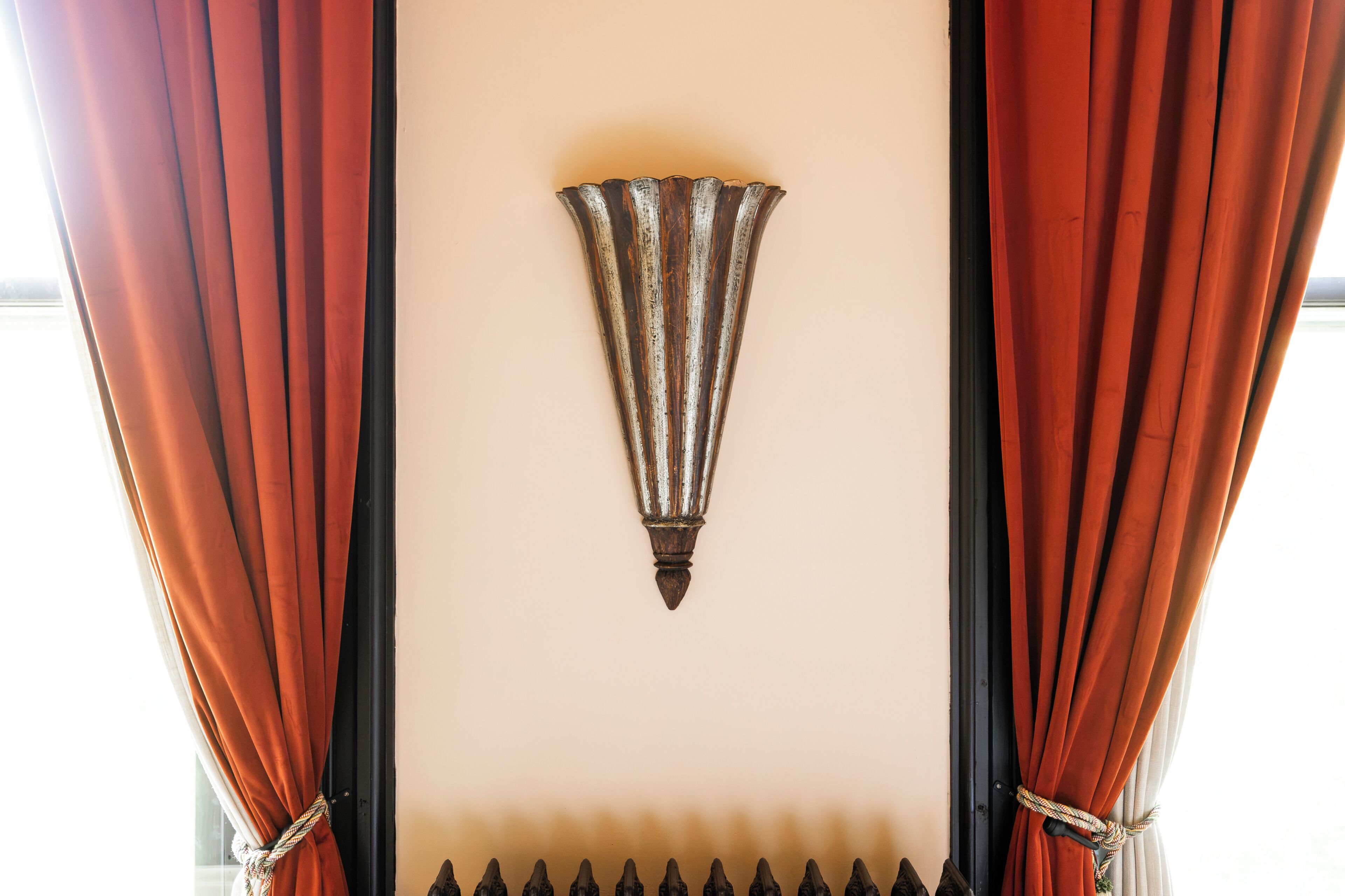 A room with a decorative wall piece, curtains, and a black metal fence.