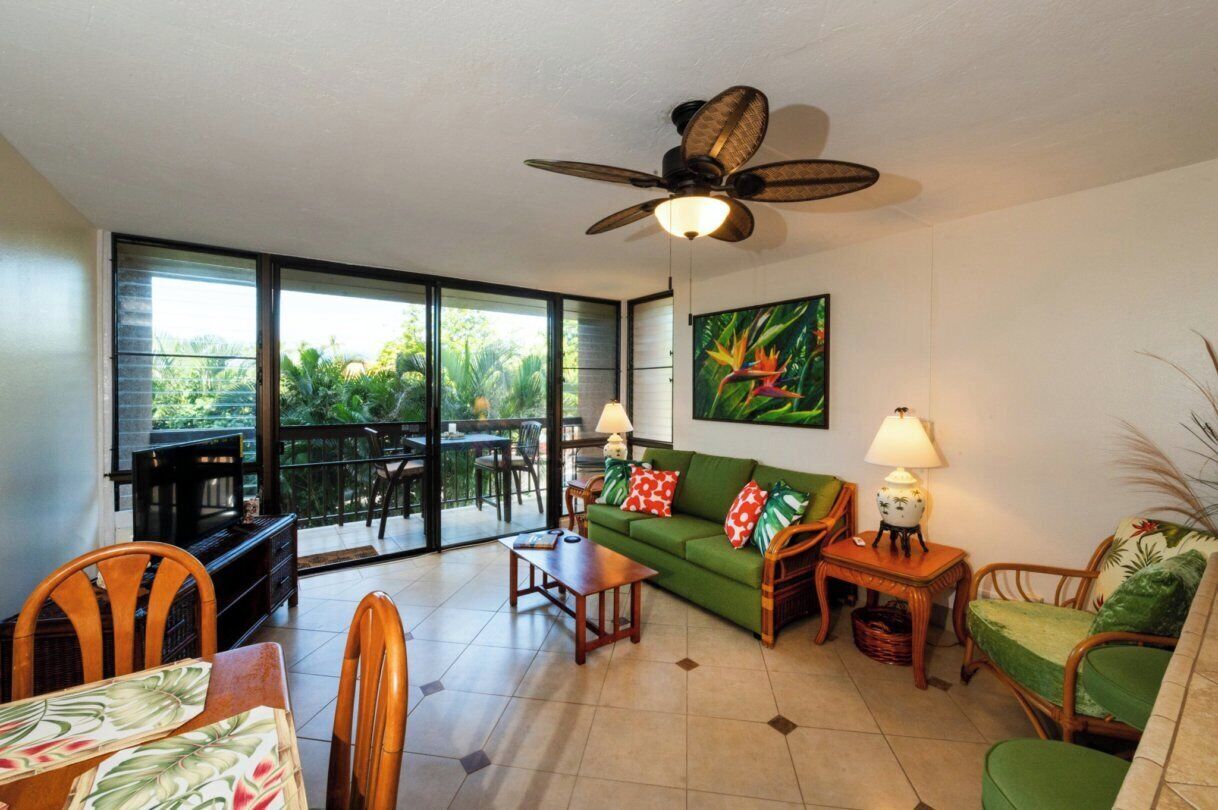 A living room with a sofa, chairs, a table, a ceiling fan, and a large window.