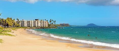 A beach with a hotel, clear skies, and ocean waves.