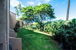 Un jardin bien entretenu, avec une variété d’arbres et d’arbustes, un ciel dégagé et un bâtiment doté d’un balcon.