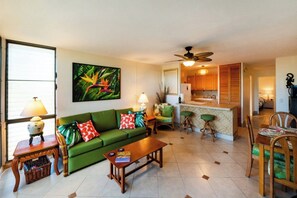A living room with a green sofa, a coffee table, and a dining area with a wooden table and chairs. - Tropical Maui Vista (Kihei)