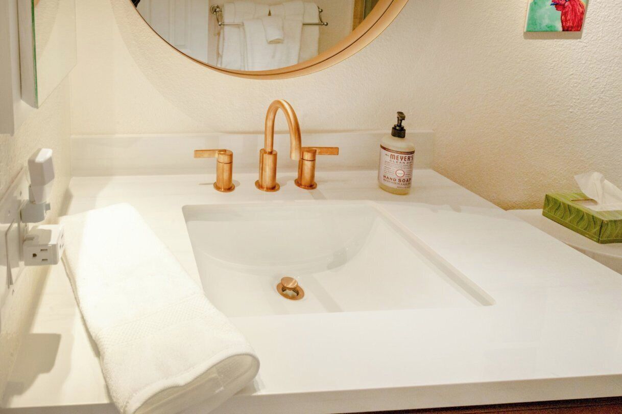 A bathroom with a white sink, a round mirror, and a hand soap dispenser.