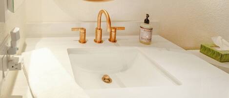 A bathroom with a white sink, a round mirror, and a hand soap dispenser.