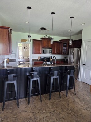 A kitchen with wooden cabinets, a stainless steel refrigerator, a microwave, and a large island with bar stools. - Our Sango Retreat (Clarksville)