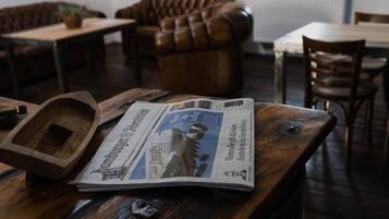 Ein Holztisch mit einer Zeitung, einem Holztablett und einem ledernen Sofa im Hintergrund.