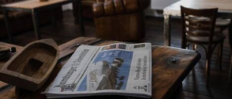 A wooden table with a newspaper, a wooden tray, and a leather couch in the background.