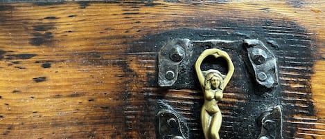 A close-up of a brass door handle with a heart-shaped design, mounted on a wooden surface with visible wear and tear.