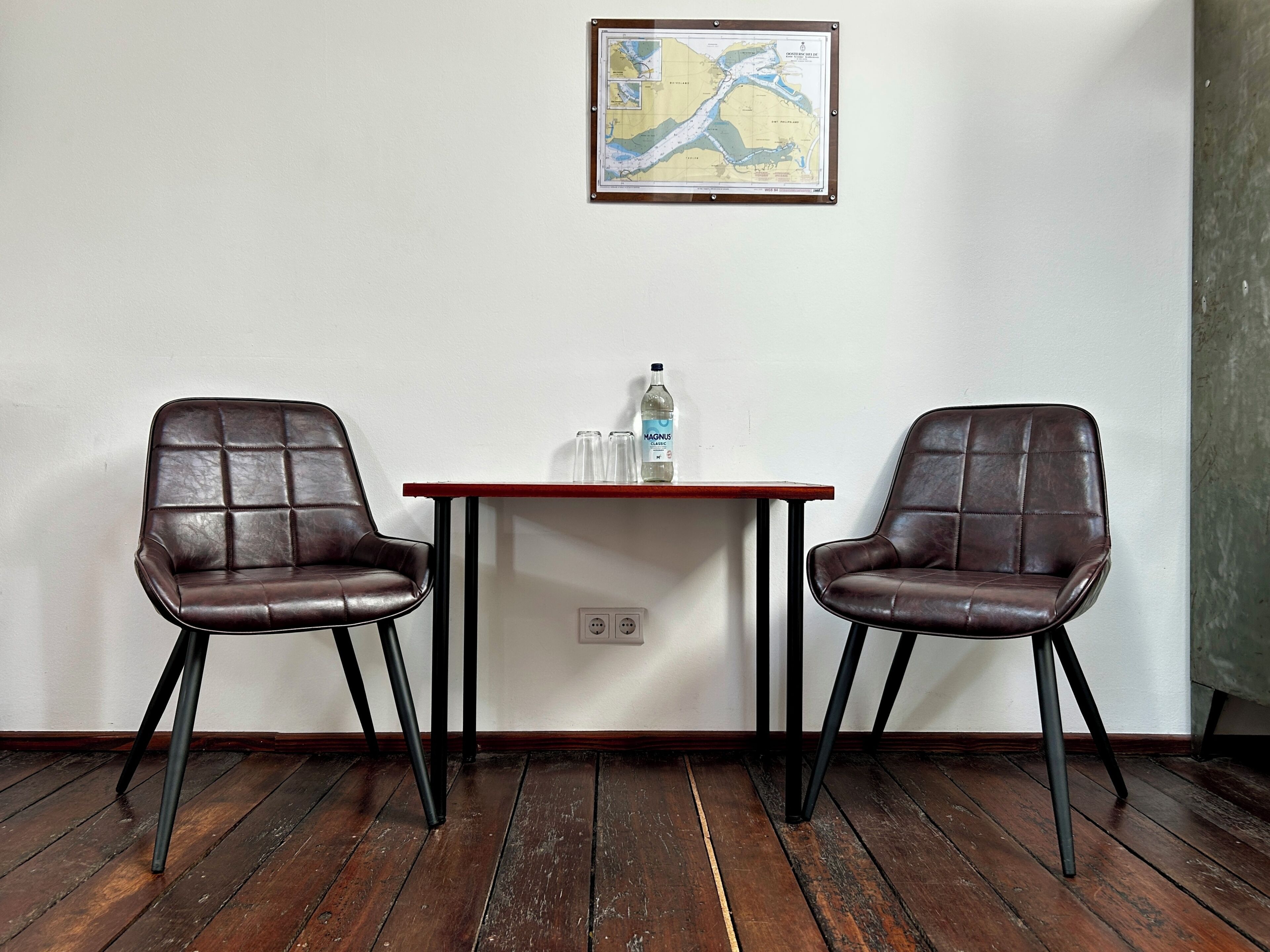 A room with two leather chairs, a wooden table, a bottle of water, and a map on the wall.