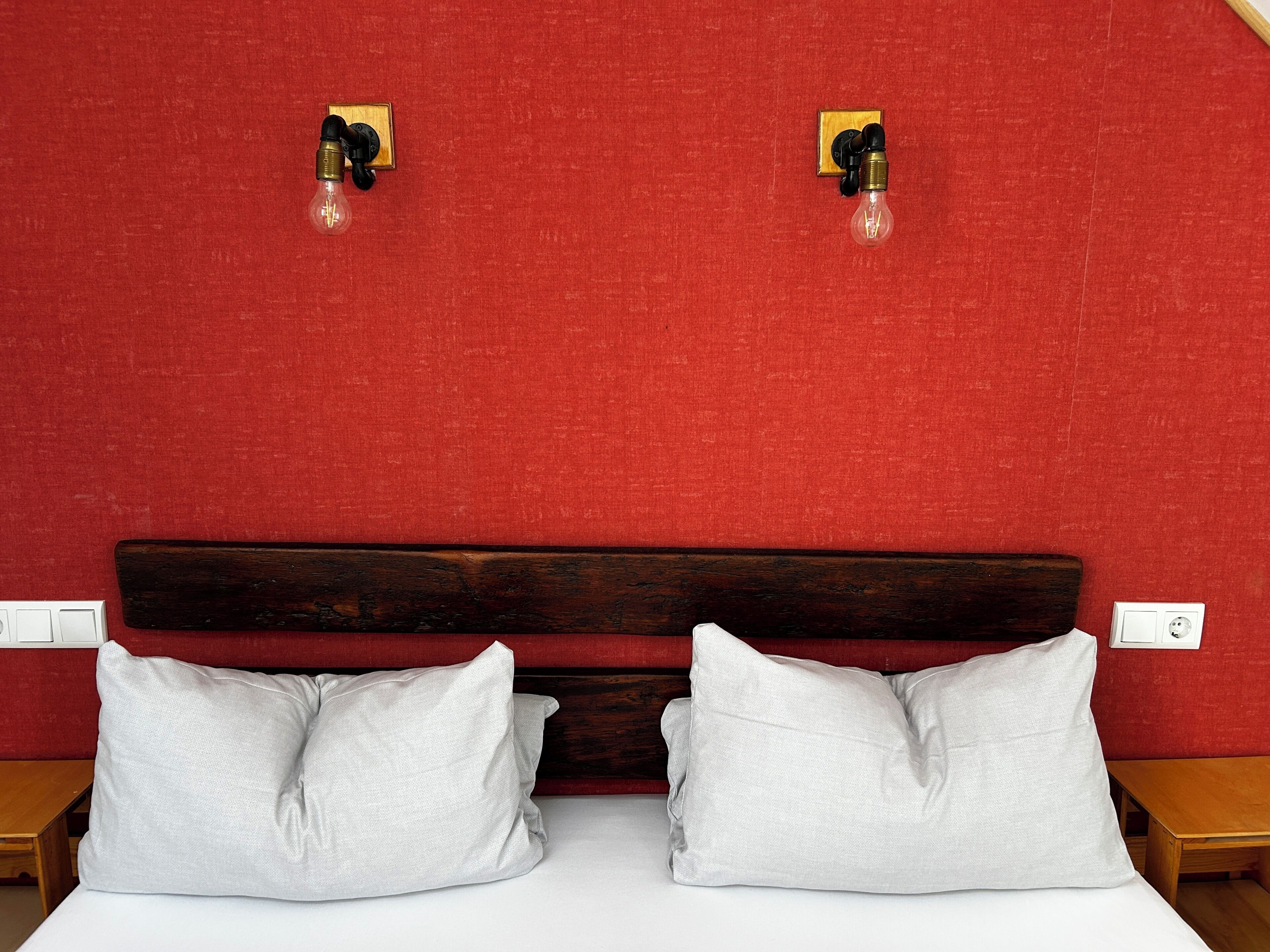Ein Bett mit weißer Bettwäsche, zwei weiße Kissen, ein hölzernes Kopfteil und zwei Wandleuchten.