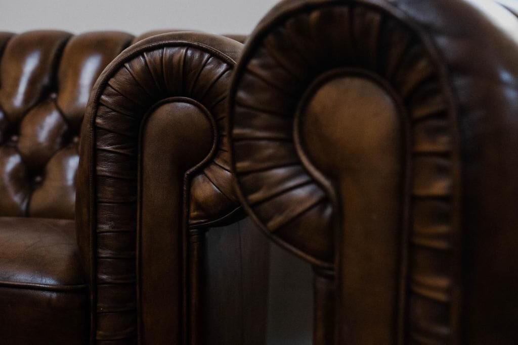 Een detailfoto van een donkerbruine leren bank met een gestuikte rugleuning en armleuningen.