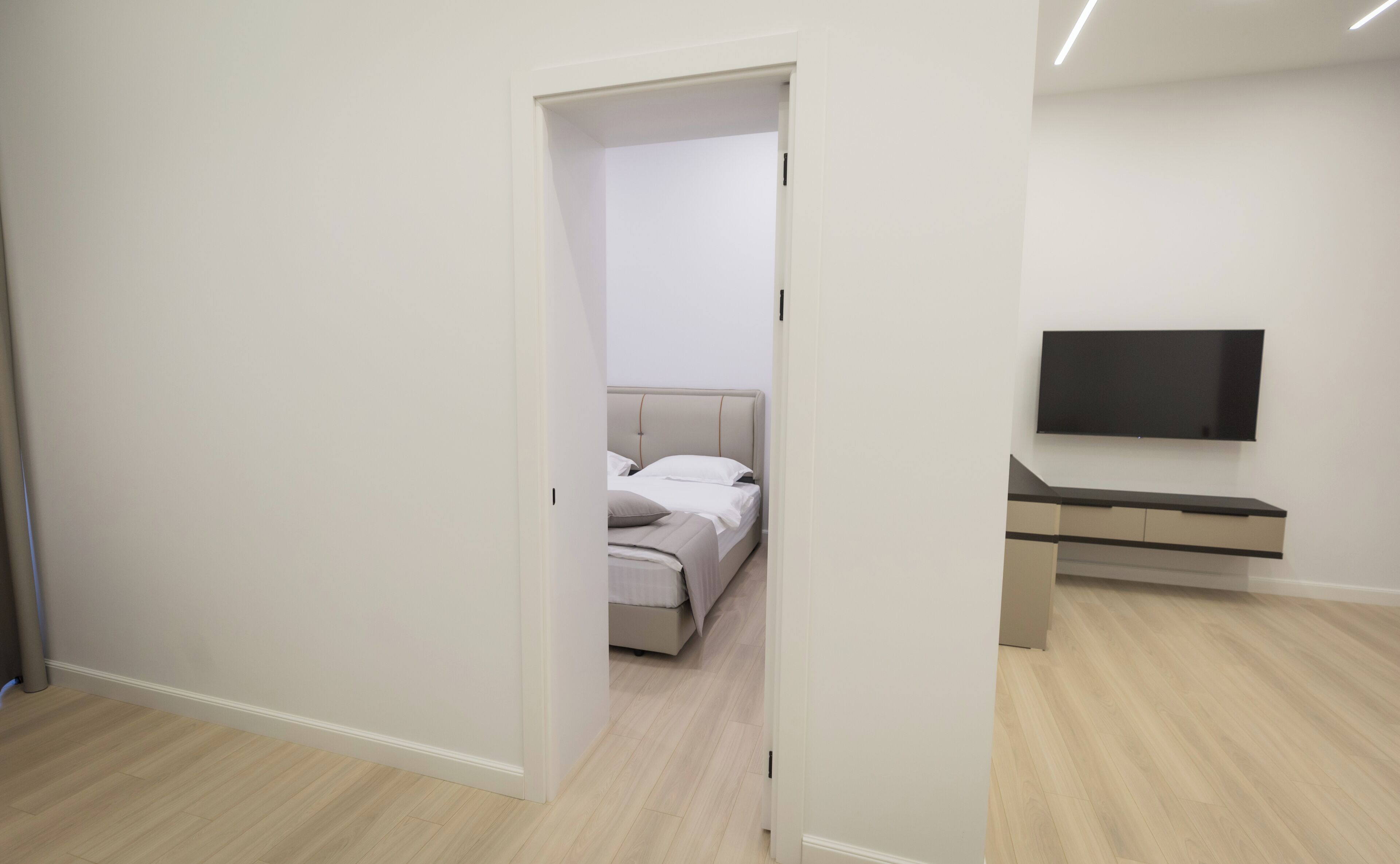 A hotel room with a bed, a TV mounted on the wall, and a wooden floor.