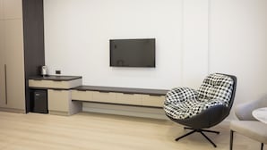Una camera moderna e minimalista con una panca integrata, una sedia nera con cuscino decorato e un televisore a schermo piatto montato a parete.