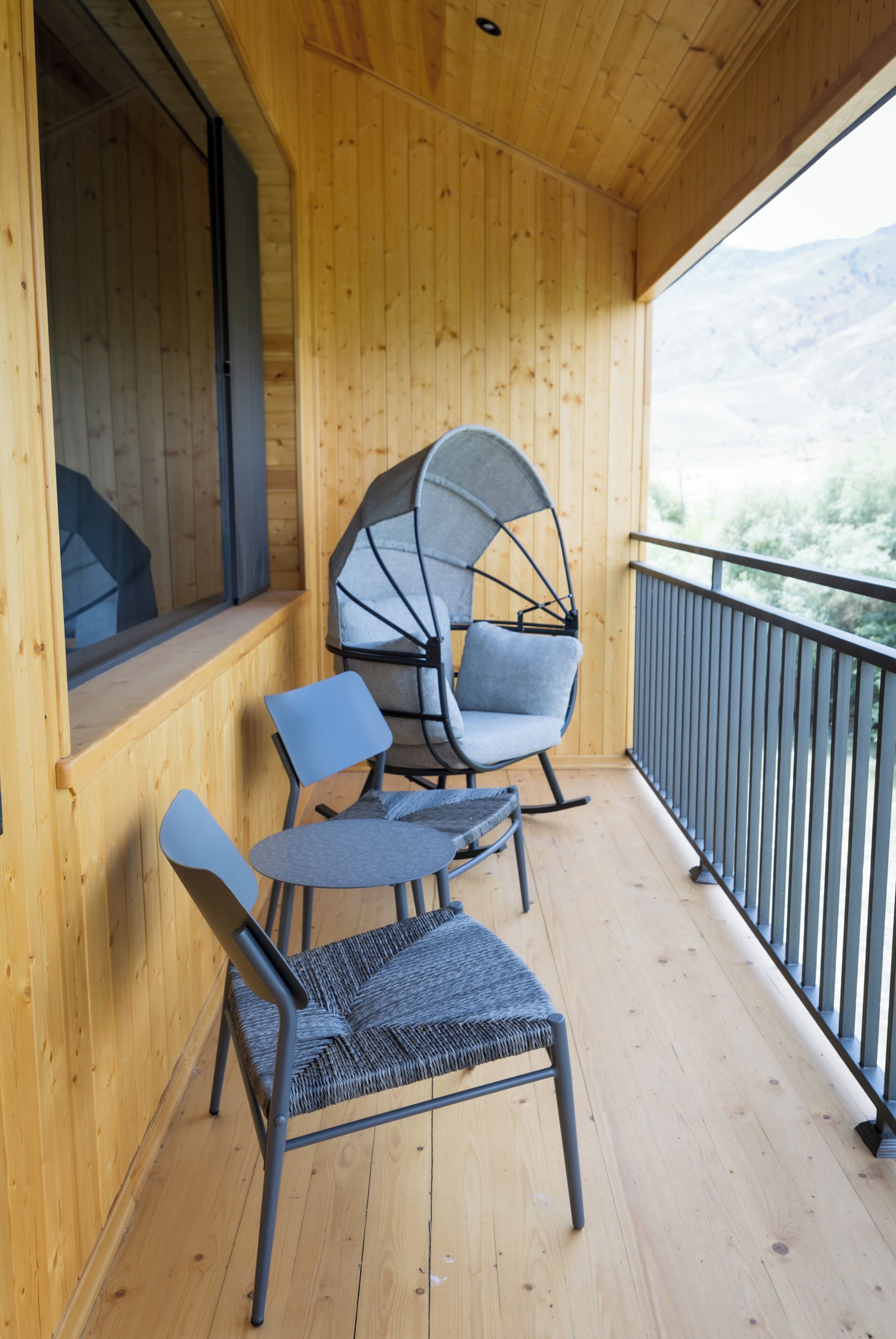 A wooden balcony with two chairs and a table, overlooking a mountainous landscape.