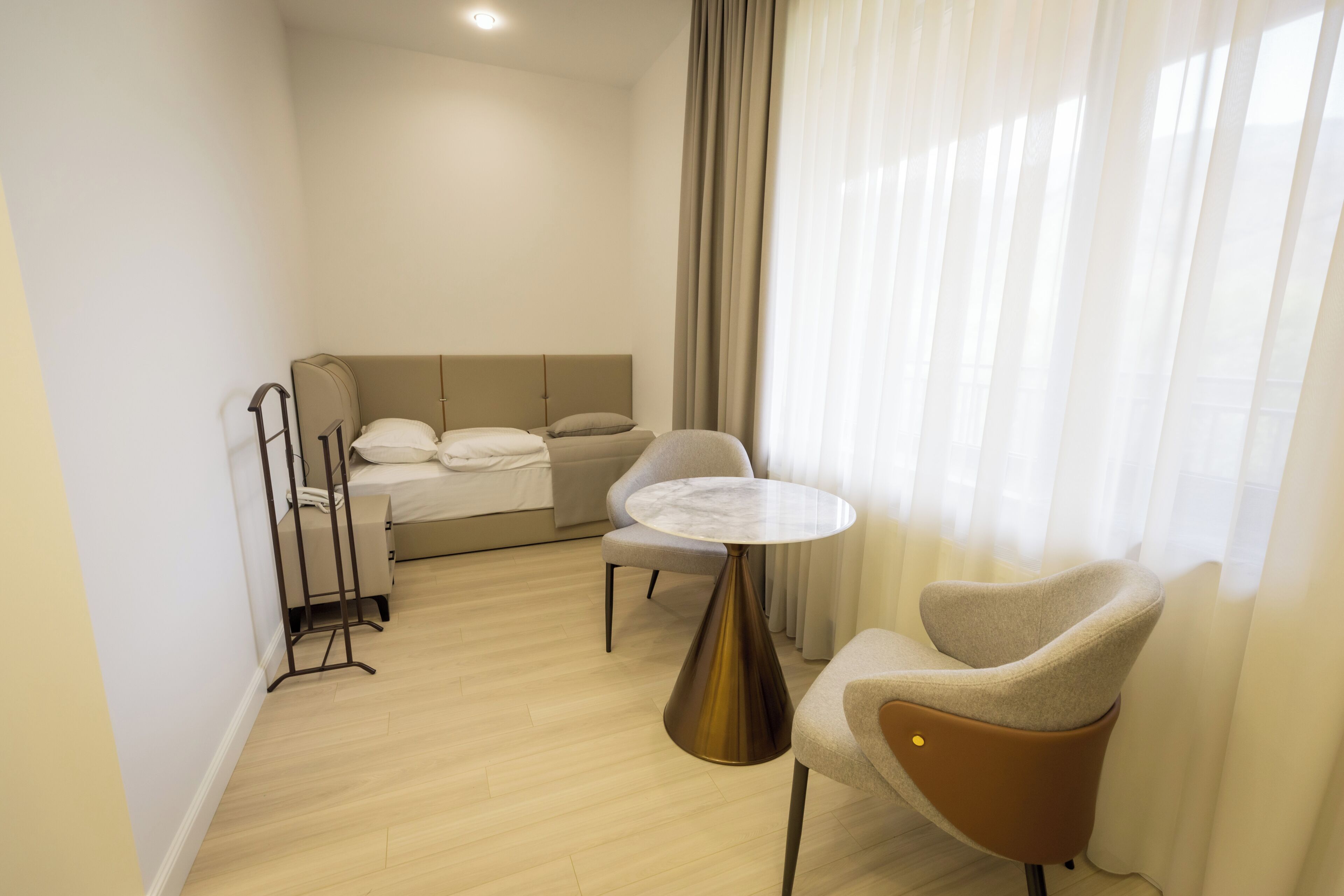 A hotel room with a bed, a bedside table, a chair, and a window with curtains.